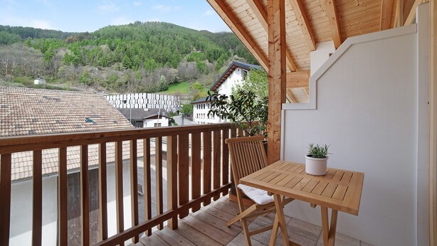 A wooden balcony with a table and chair, a potted plant, and a view of a hilly landscape. - Apartment "Zwick Valmeina" with Panoramic Views, Balcony & Shared Garden (Mals)