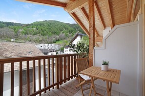 Een houten balkon met een tafel en stoel, een bloempot en uitzicht op een heuvellandschap.