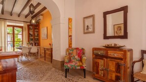 A cozy living room with a patterned armchair, a wooden cabinet, and a dining area with a table and chairs.