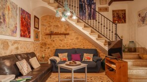 A cozy living room with a stone wall, a staircase, a leather sofa, a coffee table, and various artworks.