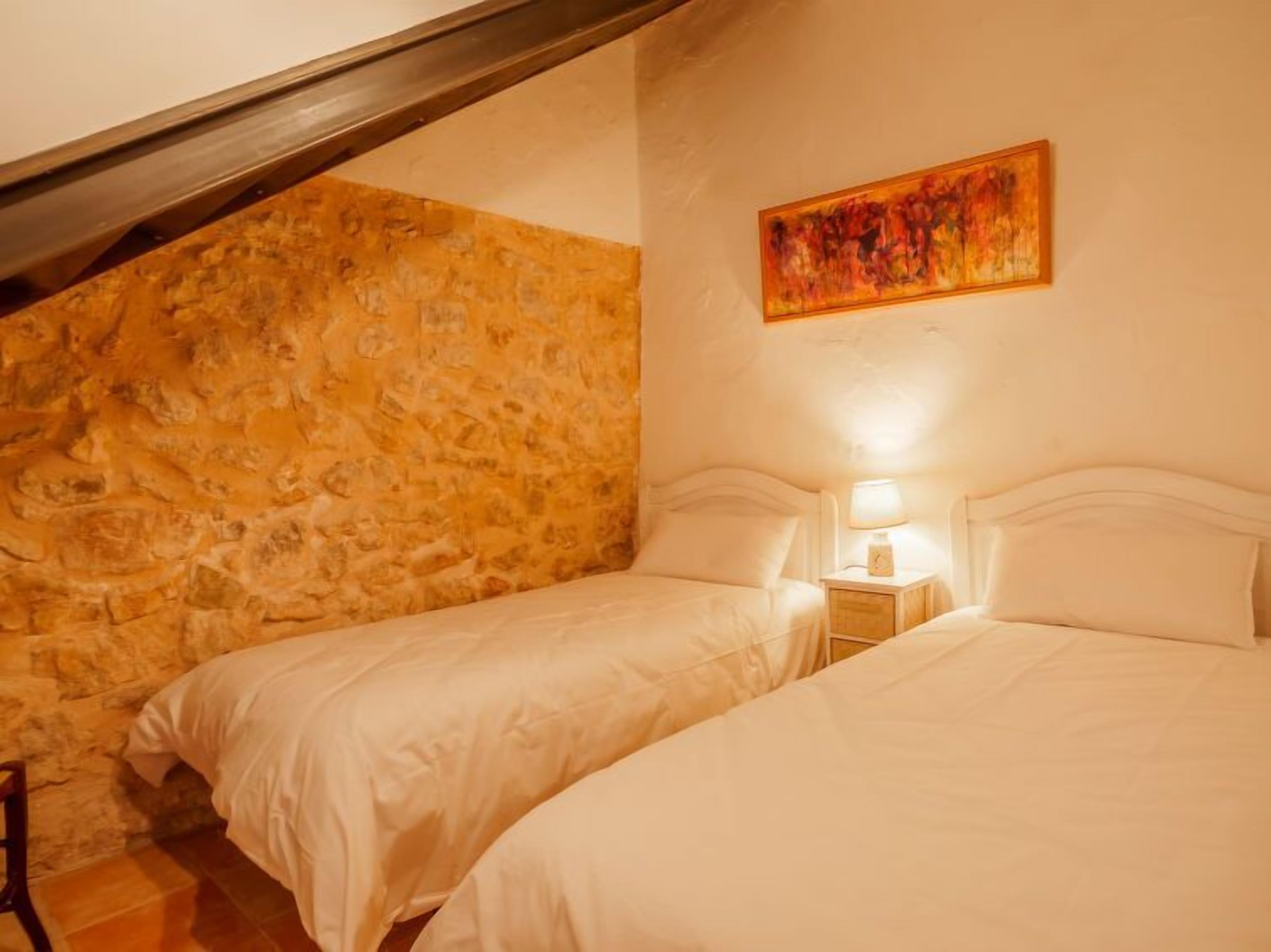 A bedroom with two beds, a stone wall, a wooden beam, and a painting.