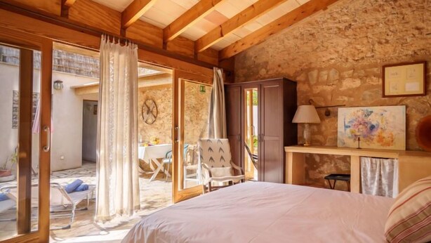 A bedroom with a bed, a desk, a chair, and a stone wall.