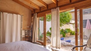 A bedroom with a bed, wooden ceiling beams, and a sliding glass door leading to an outdoor area with a chair and a table.