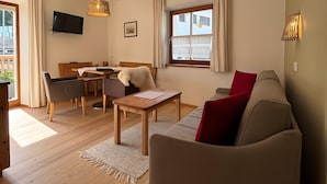 A living room with a sofa, a table, a TV, and a window with curtains. - Holiday Apartment "Zwick Spinei" with Mountain View, Balcony & Shared Garden (Mals)