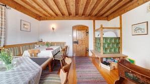 A room with a wooden ceiling, a dining table with chairs, a bench, a bed, and a green storage unit. - Holiday Apartment "Zwick Spinei" with Mountain View, Balcony & Shared Garden (Mals)