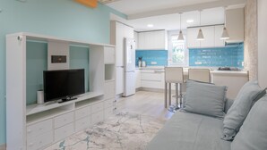 Una cucina moderna con mobili bianchi, TV integrata e schienale blu.