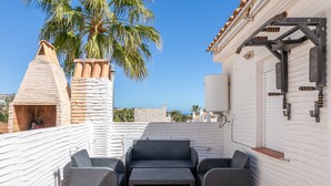 Una terrazza sul tetto con un'area salotto, una parete bianca con motivo decorativo e una palma.