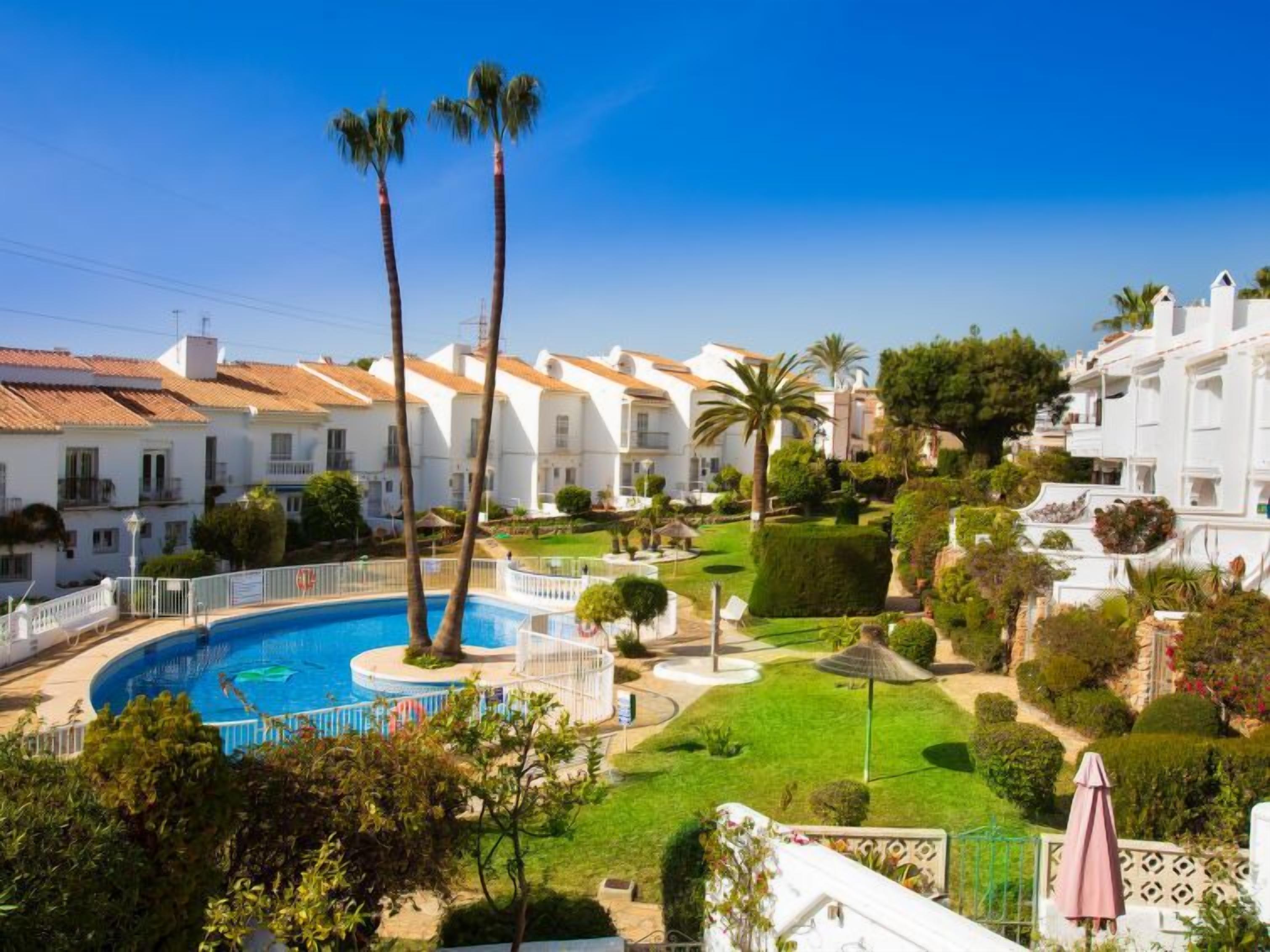 Ein Resort mit Swimmingpool, Palmen und weißen Gebäuden mit roten Ziegeldächern.