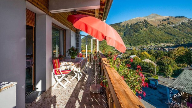 A balcony with a wooden railing, a table with chairs, and a red umbrella.