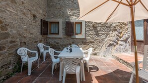 Un bâtiment en pierre doté d’un patio comprenant une table et des chaises, une bouteille de vin et un grand parasol.