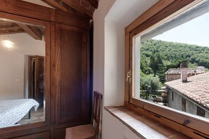 A room with a wooden wardrobe, a bed with a patterned bedspread, and a window overlooking a forested area.