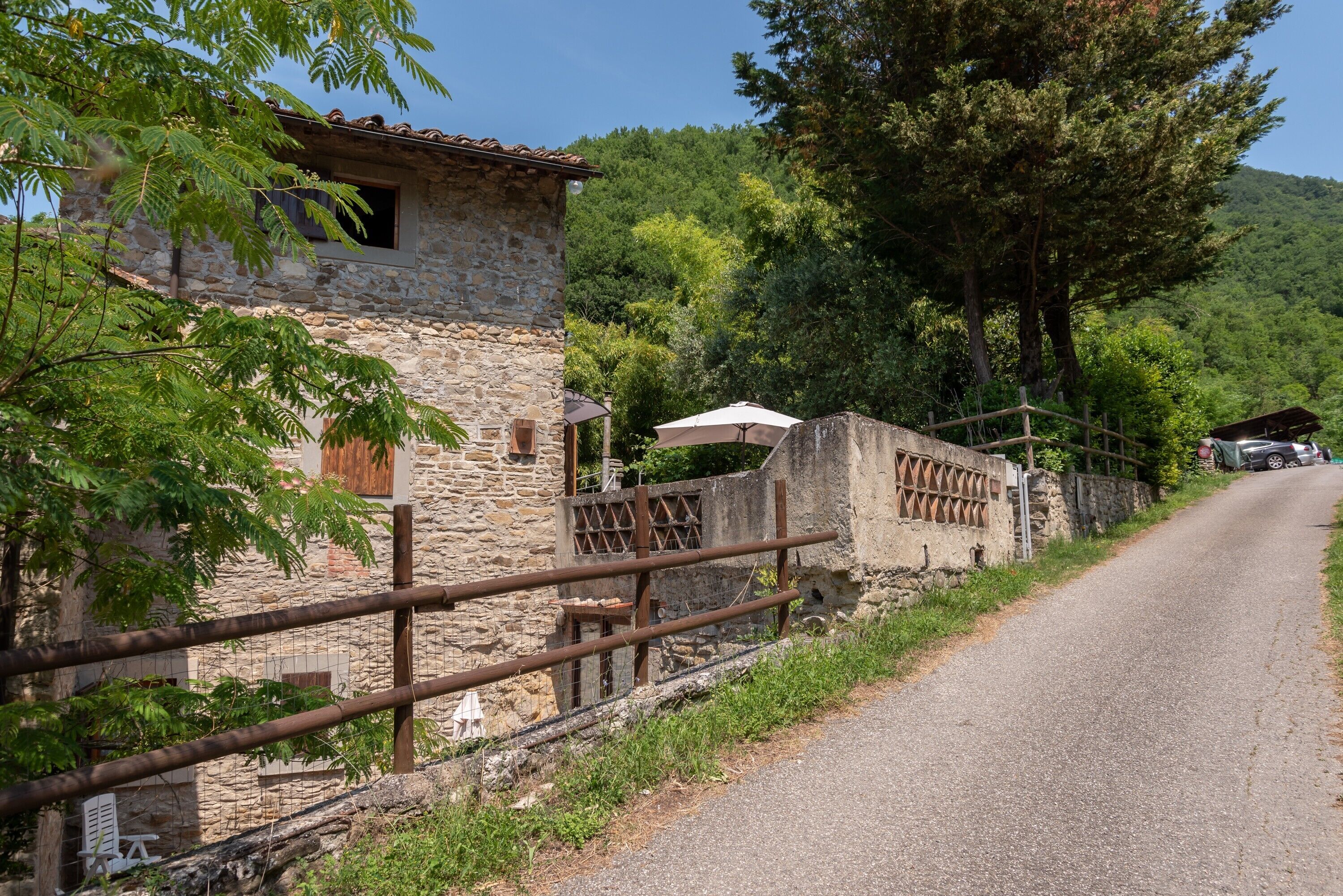 A stone building with a rustic appearance, a paved road, and a forested hillside in the background.