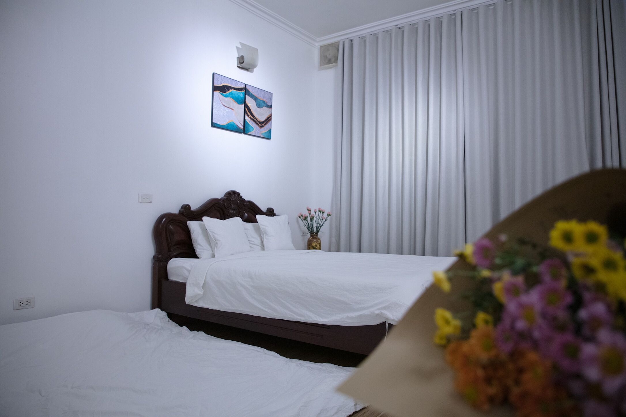 Una habitación de hotel con una cama, una mesita de noche, un florero con flores y un cuadro en la pared.