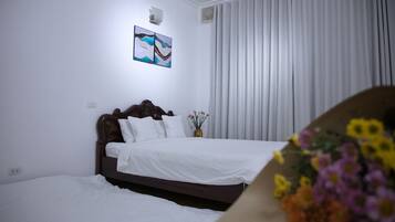 Una habitación de hotel con una cama, una mesita de noche, un florero con flores y un cuadro en la pared.
