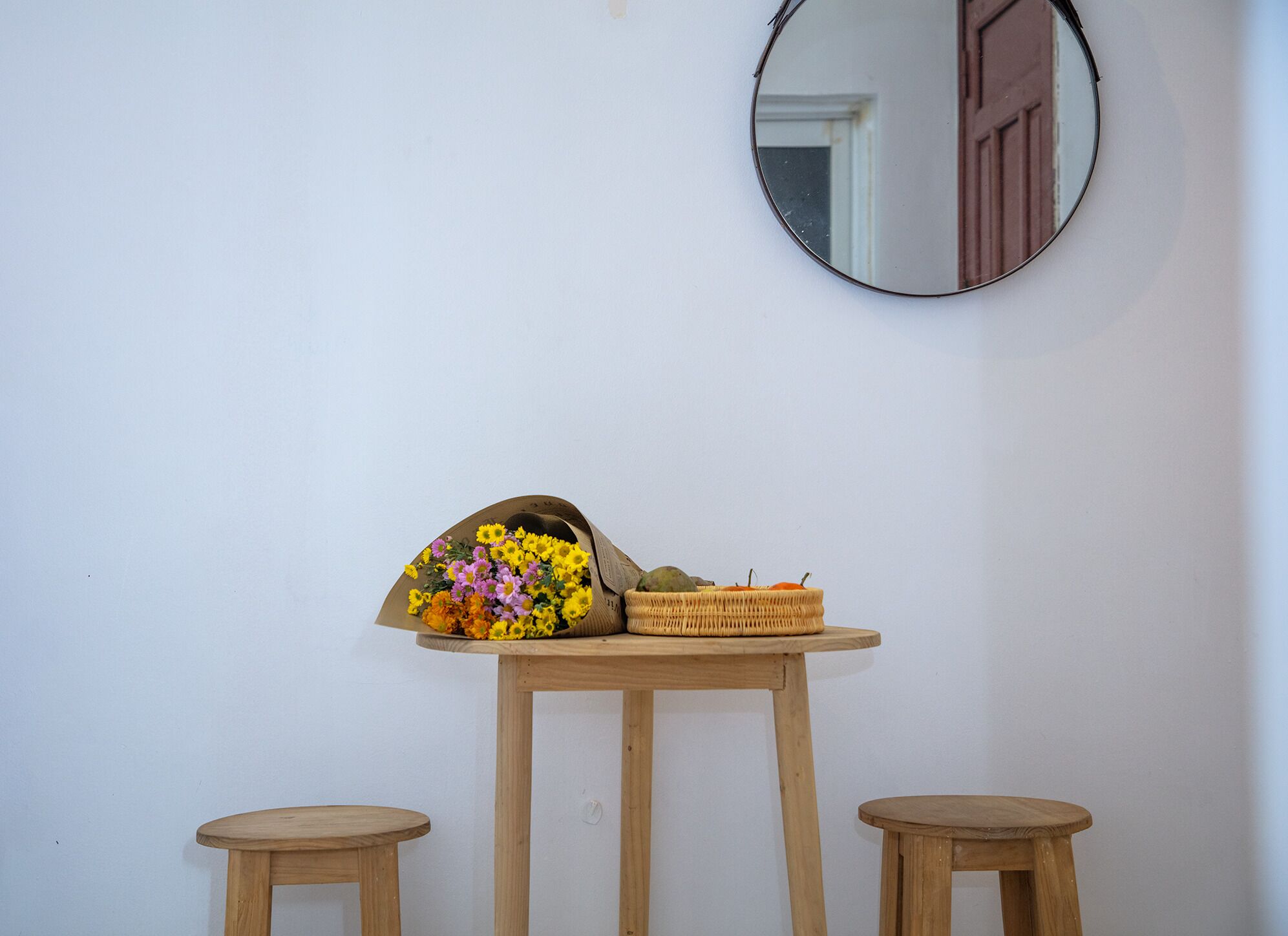 Une petite table en bois, un miroir accroché au mur, un panier en osier et un bouquet de fleurs.
