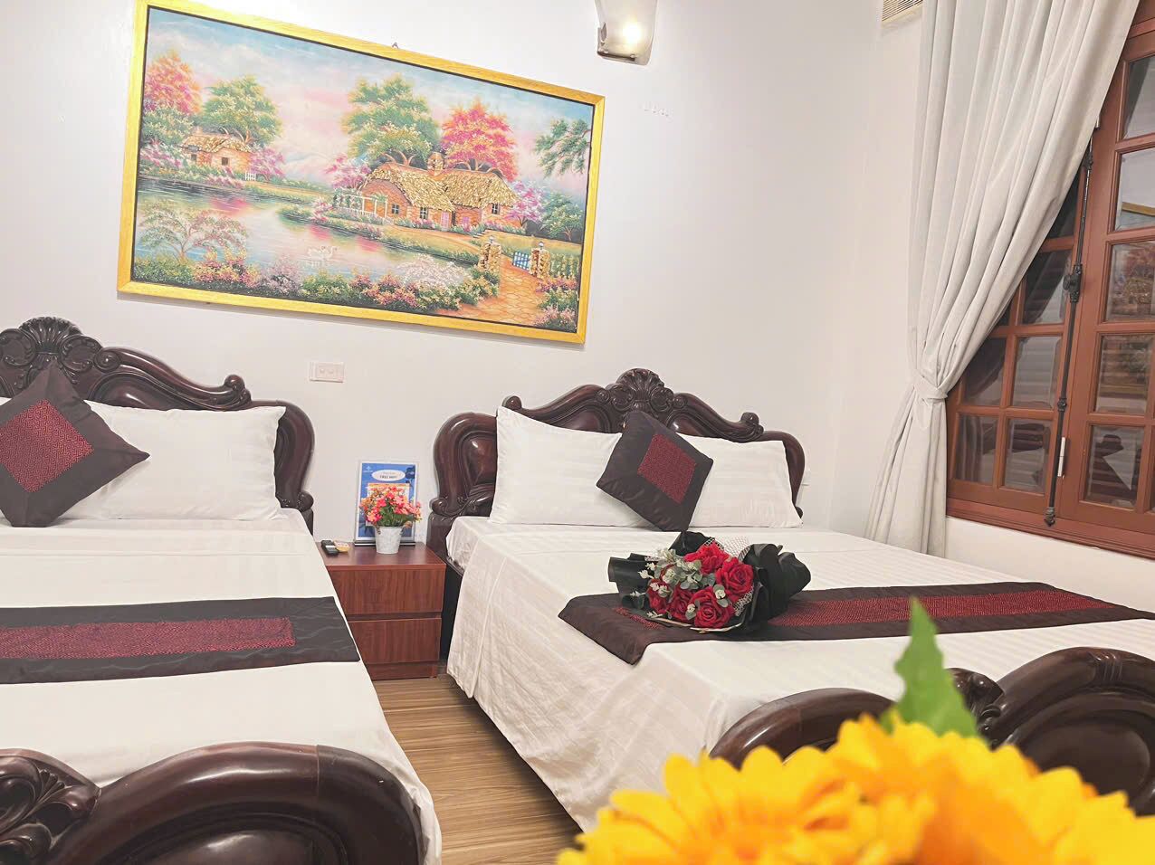 Habitación de hotel con dos camas, un cuadro de un paisaje y un ramo de flores sobre la cama.