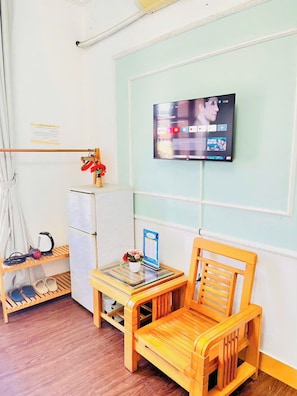 A room with a wooden chair, a small table, a TV mounted on the wall, a shelf with shoes, and a hanging coat rack.