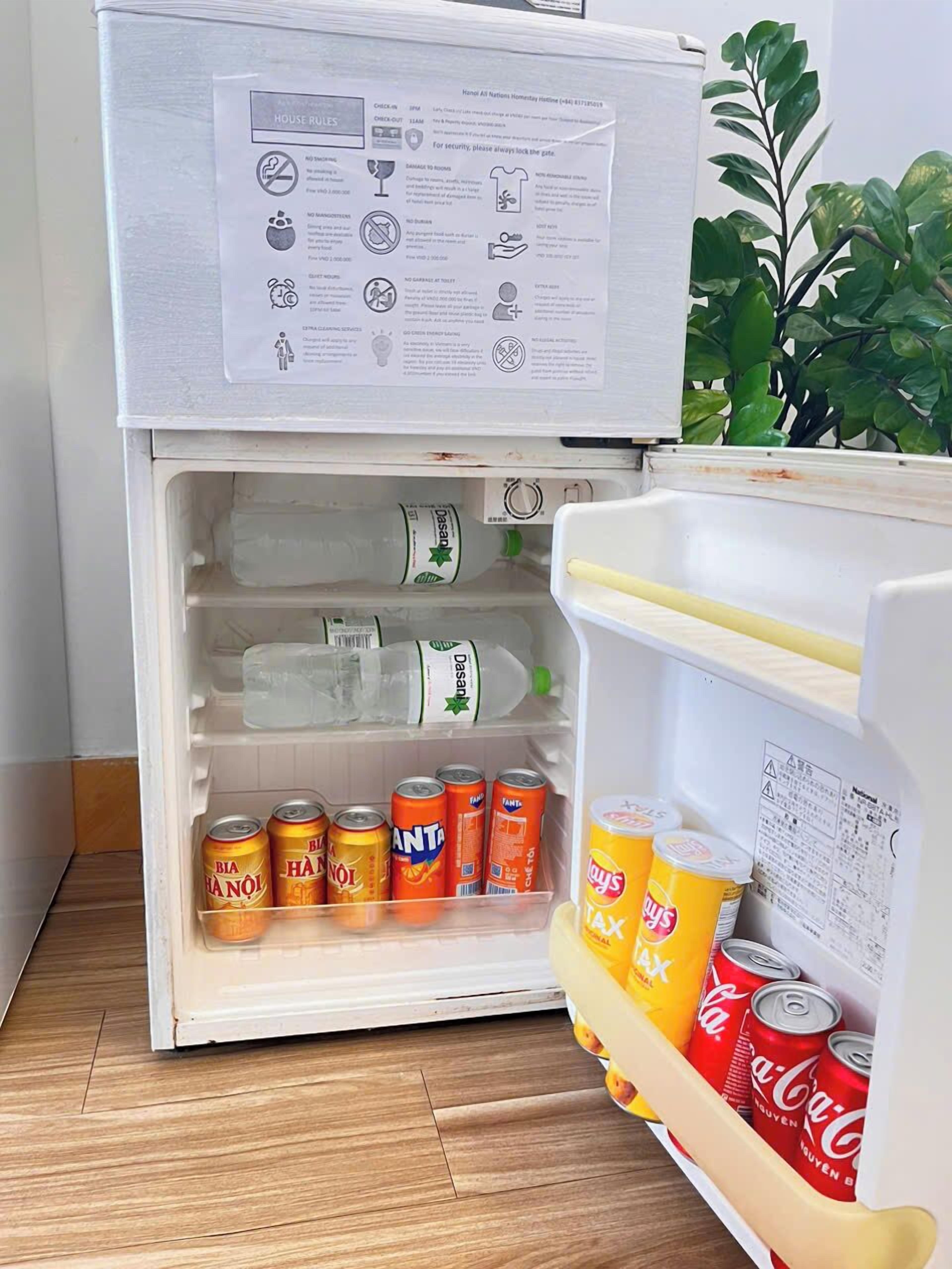 Ett kylskåp med en bruksanvisning på dörren, och inuti finns drycker som Bia Hanoi, Fanta och Coca-Cola.