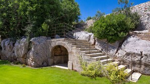 Una escalera de piedra conduce a un arco de piedra, rodeado de vegetación y un cielo azul despejado.