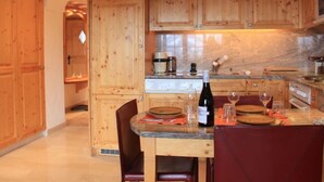 A wooden kitchen with a marble countertop, wooden cabinets, and a dining table set for two. - Dauphin 7 by Interhome (Villars)