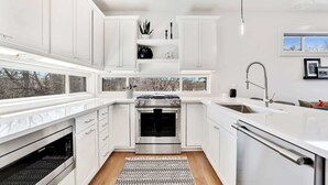 Een moderne keuken met witte kasten, een ingebouwde oven, een vaatwasser en een raam met uitzicht op bomen.