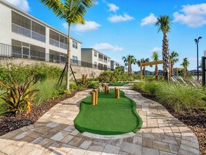 A golf putting green with a hole, surrounded by palm trees and a building with balconies.