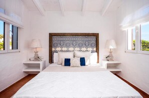 A bedroom with a large bed, two bedside tables, a patterned headboard, and windows on both sides. - Villa 'Bini Sek' with Sea View, Private Terrace and Air Conditioning (Binibèquer)