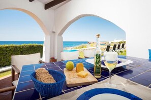 A table with a bottle of BLANCO DOLOZA, a glass of white wine, a basket of bread, and a cutting board with cheese and lemon. - Villa 'Bini Sek' with Sea View, Private Terrace and Air Conditioning (Binibèquer)