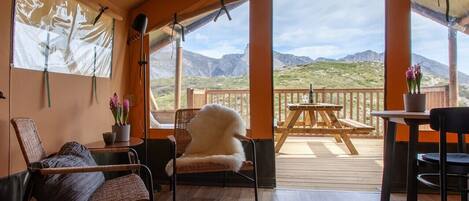 Una habitación acogedora con sillones de mimbre, un tapete redondo y vistas a las montañas a través de amplios ventanales.