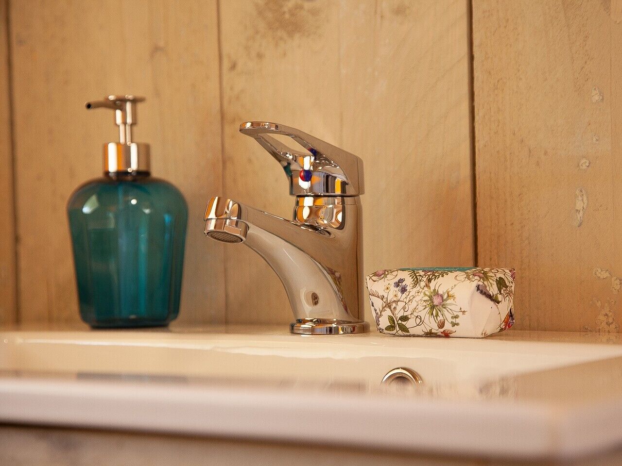 Un lavabo de salle de bain doté d’un robinet moderne, d’un distributeur de savon et d’un porte-savon orné d’un motif floral.