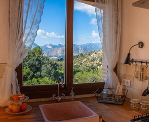 A kitchen with a sink, a fruit tray, and a view of mountains through the window.
