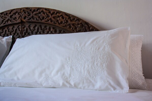 A neatly made bed with a white pillow featuring embroidered floral patterns and a textured white pillowcase.