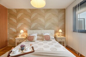 Een hotelkamer met een groot bed, twee nachtkastjes met lampen, een raam met gordijnen en een kamer met een patroon op de muur.