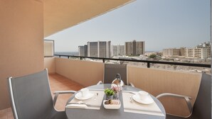 A balcony with a table set for two, a chair, and a view of the cityscape. - Vacation Home "Vista Paraiso" with Sea View, Shared Pool & Wi-Fi (Adeje)