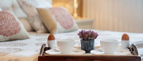 A breakfast tray with two cups and two eggs on a bed with a floral bedspread and pillows.
