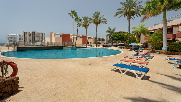 A pool area with lounge chairs, palm trees, and a view of high-rise buildings. - Vacation Home "Vista Paraiso" with Sea View, Shared Pool & Wi-Fi (Adeje)