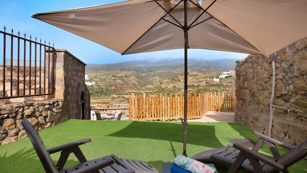Une terrasse avec un revêtement de gazon synthétique, deux fauteuils et un grand parasol.
