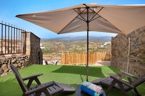 A terrace with artificial grass, two lounge chairs, and a large umbrella.