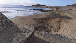 Un paysage côtier avec une plage, un terrain rocheux et des collines à l’horizon.