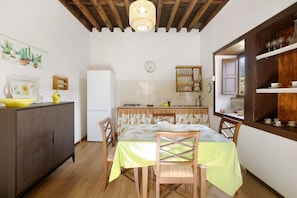A kitchen with wooden cabinets, a dining table with chairs, a refrigerator, and a hanging light fixture.