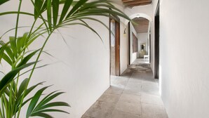 Un couloir aux murs blancs, doté d’un sol carrelé et de poutres en bois au plafond.