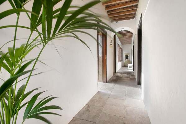 A corridor with white walls, a tiled floor, and wooden ceiling beams.