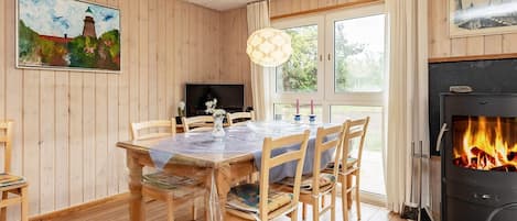 Une pièce chaleureuse avec un décor intérieur en bois, une table à manger avec des chaises, une cheminée et un téléviseur.