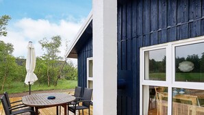 A wooden deck with a round table and chairs, an umbrella, and a view of a green landscape. - 6 Person Holiday Home in Laeso (Læsø)