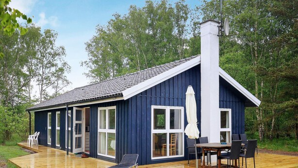 A blue cabin with a wooden deck, a dining area with chairs and a table, and a chimney. - 6 Person Holiday Home in Laeso (Læsø)