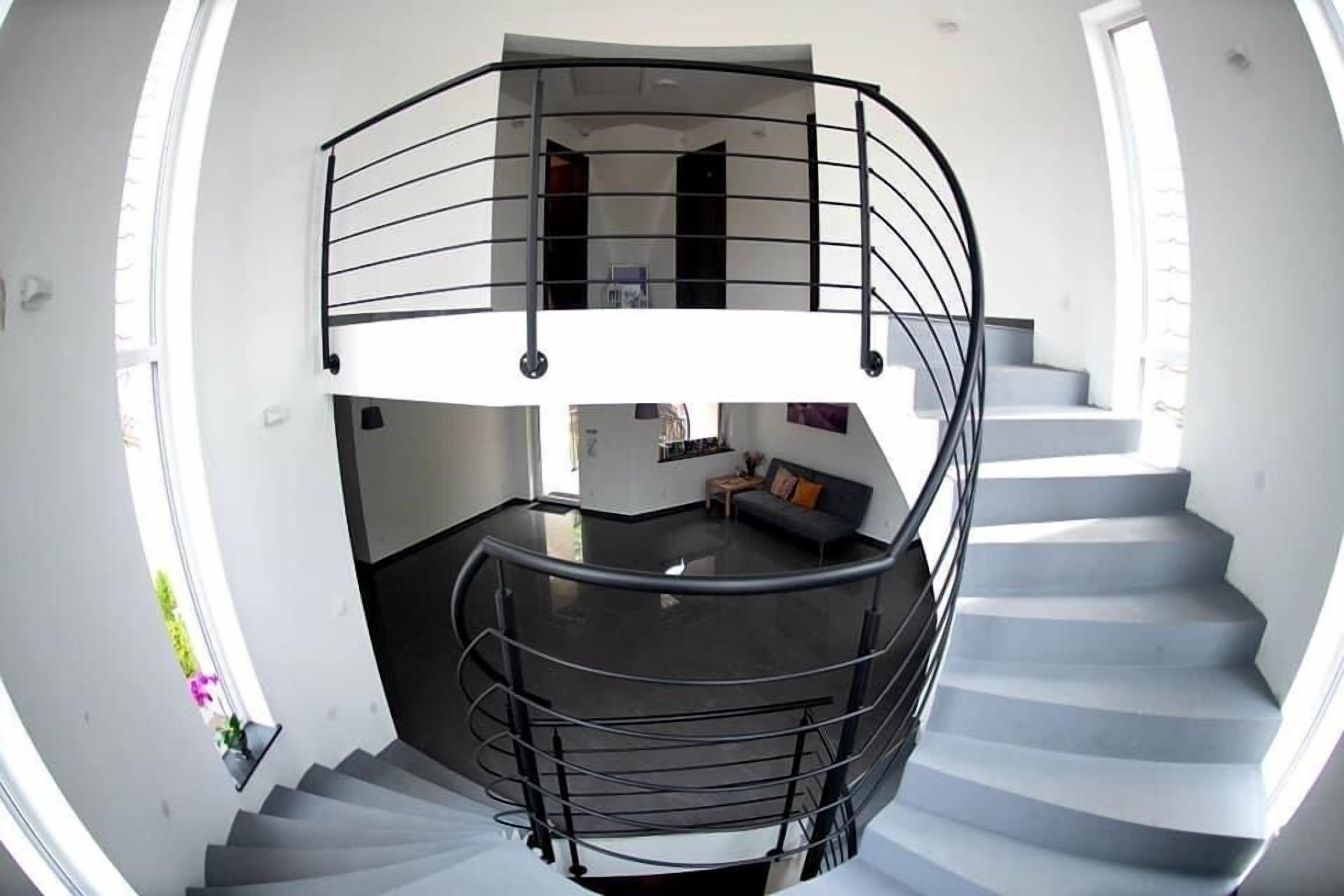 A modern spiral staircase with a black railing, leading to a second-floor balcony with a view of the interior.