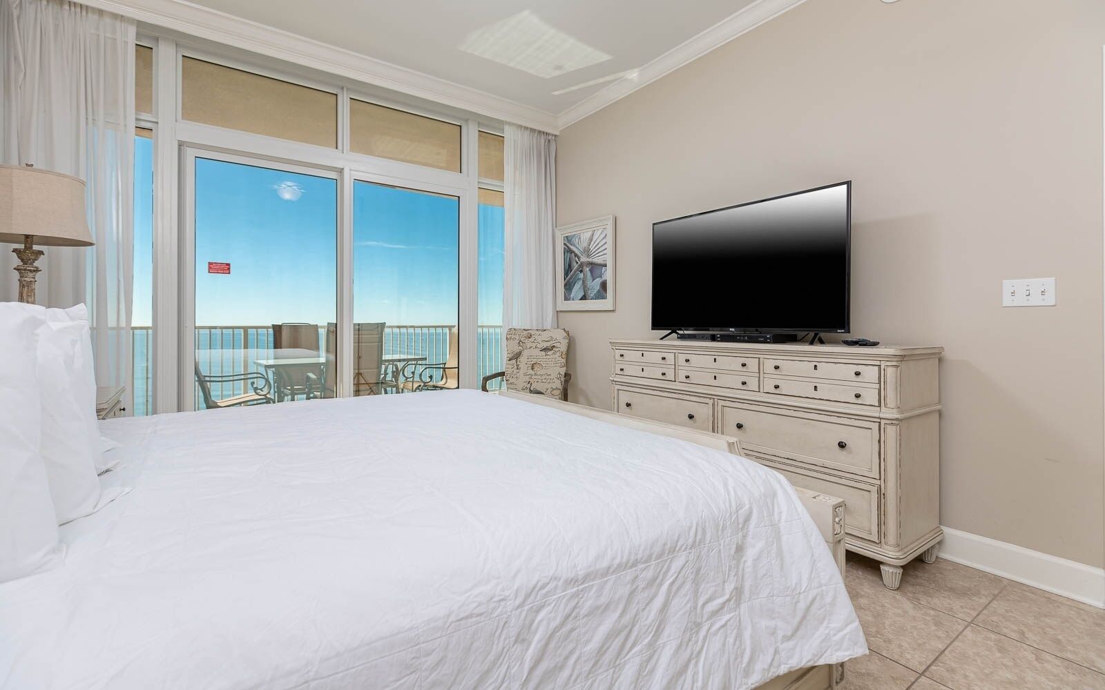 A hotel room with a large bed, a television on a dresser, and a balcony with a view.