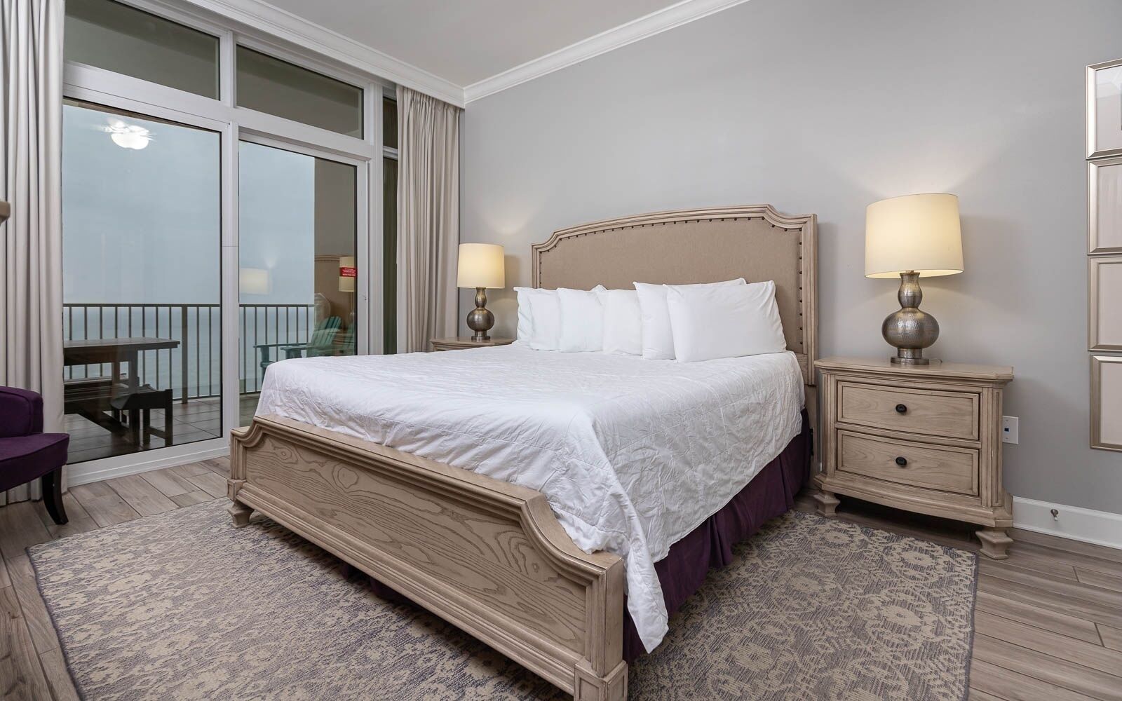 A bedroom with a large bed, two bedside tables, a chair, and a balcony with a view.