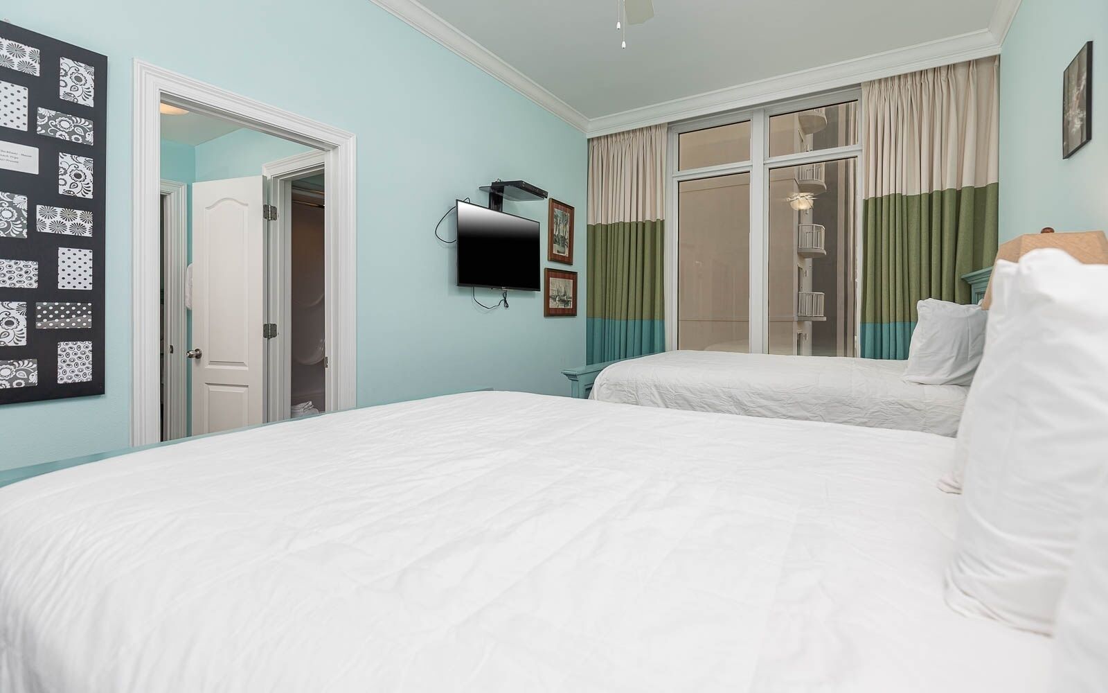 A bedroom with two beds, a TV, a wardrobe, and a window with curtains.