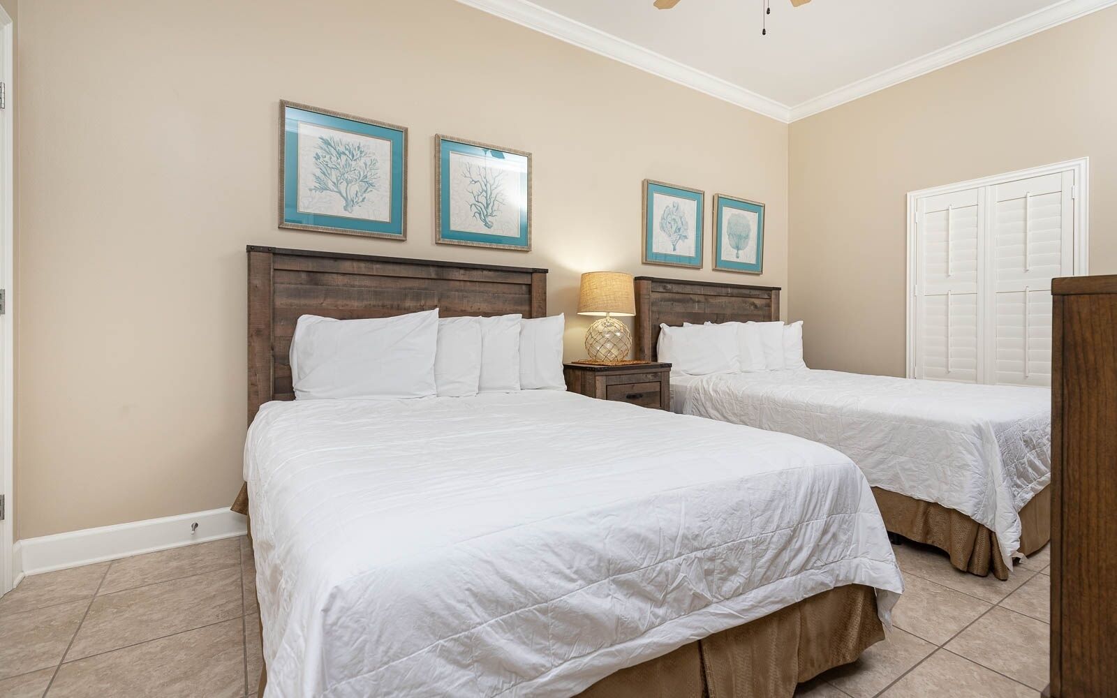 A hotel room with two beds, a wooden headboard, a nightstand with a lamp, and framed artwork on the wall.